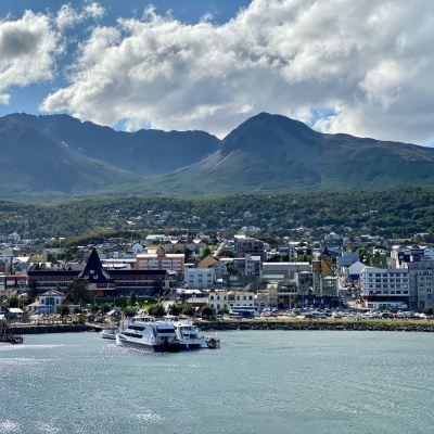 Cidade costeira com montanhas ao fundo, céu nublado e barcos no mar