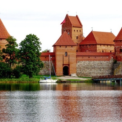 Castelo medieval de pedra com telhados vermelhos junto a lago e árvores