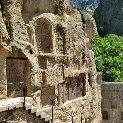 Paredes rochosas com portas e relevos talhados e escadaria exterior em ambiente montanhoso