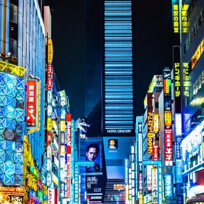 Rua urbana noturna com muitos letreiros luminosos coloridos e pessoas a atravessar passadeira