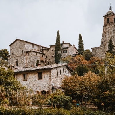 Conjunto de casas de pedra com teto de telha vermelha e torre alta rodeadas por árvores