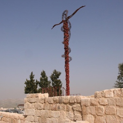 Escultura de cristo em metal vermelho-ferrugem sobre parede de pedra clara