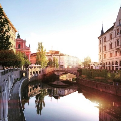 Canal urbano com edifícios históricos, árvores, esplanadas e ponte ao pôr do sol