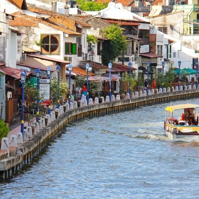 Barco turístico amarelo e vermelho num rio com passeio pedonal e edifícios antigos coloridos ao largo.