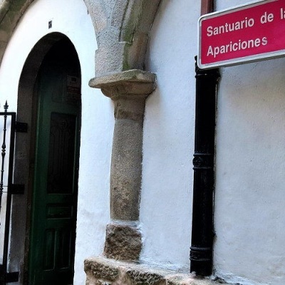 Porta verde arqueada numa parede branca com portão de ferro e sinal 'Santuario de las Apariciones'