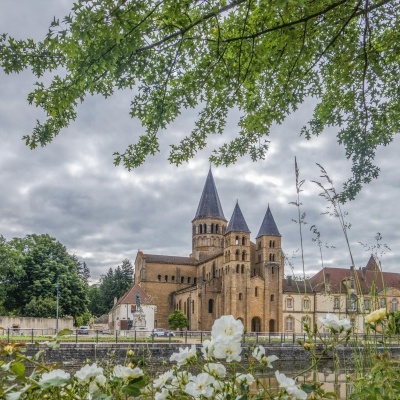 Igreja antiga de pedra com três torres e flores brancas ao primeiro plano
