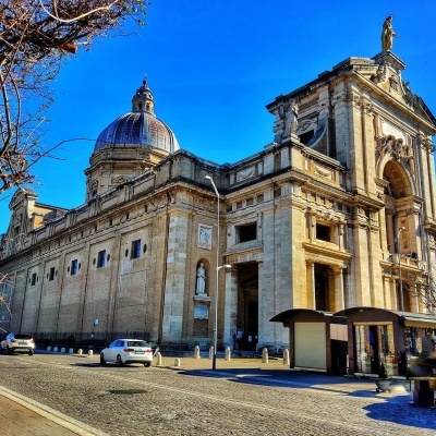 Edifício histórico em pedra com cúpula e estátuas na rua com carros e quiosque