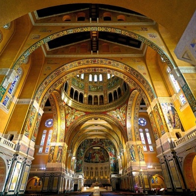 Interior de catedral com arcos dourados, vitrais coloridos e colunas brancas