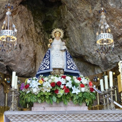 Altar com estátua religiosa, flores, candelabros e lustres numa gruta