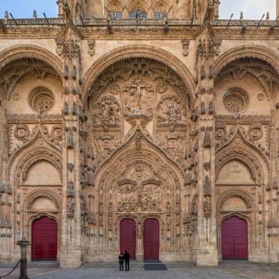 Fachada gótica de pedra com três portas vermelhas e detalhamento arquitetónico