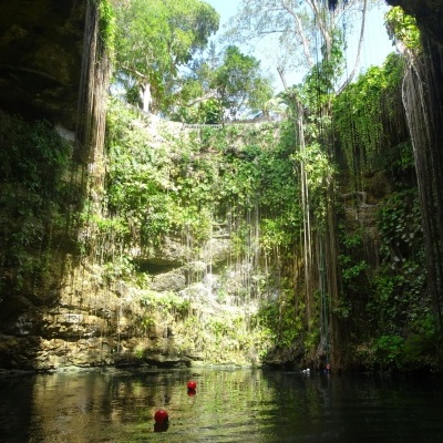 Cenote natural com água clara e vegetação nas paredes rochosas