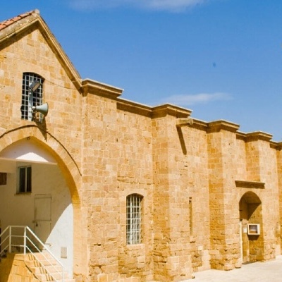 Edifício histórico em pedra amarela com arcos e torre sineira sob céu azul