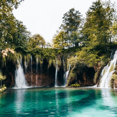 Cascatas a cair em lago azul rodeado por vegetação verde