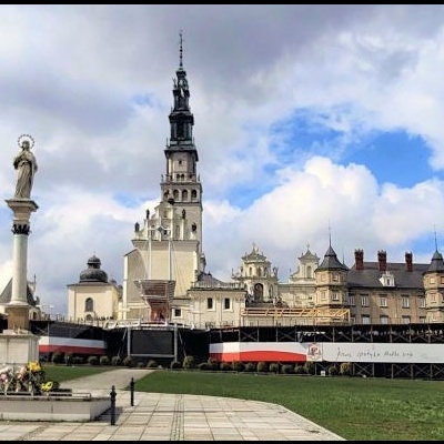Praça com estátua e edifício histórico ao fundo sob um céu parcialmente nublado