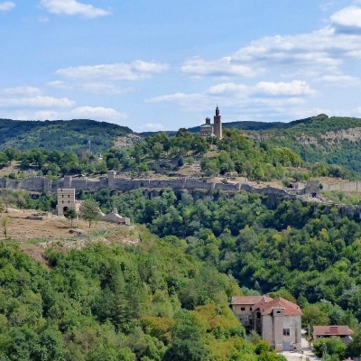 Vila antiga com castelo no topo de uma colina verde sob um céu azul com nuvens