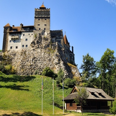 Castelo antigo no topo de colina rochosa com casa de madeira e bandeiras em área verde