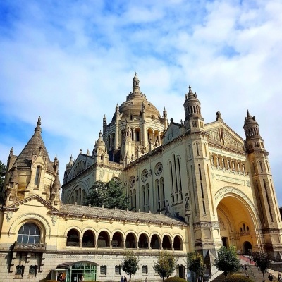 Edifício histórico com torres e cúpulas em pedra clara sob céu azul com nuvens
