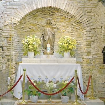 Altar religioso com estátua dourada, plantas amarelas e toalha branca em parede de pedra