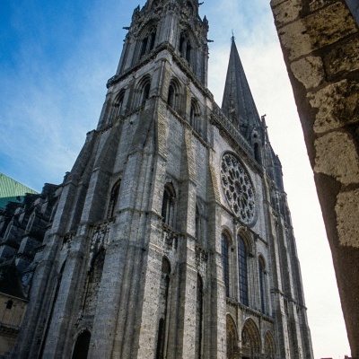 Edifício gótico em pedra com torre alta e rosácea circular, céu azul
