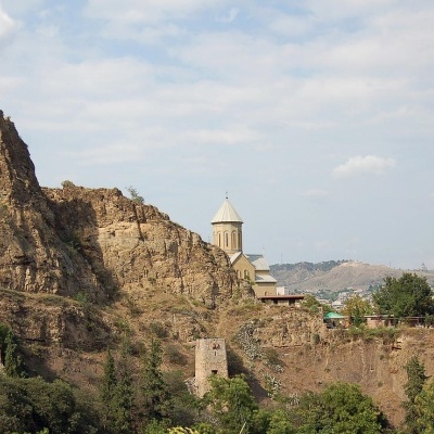 Castelo antigo de pedra numa colina com torres e um edifício com cúpula