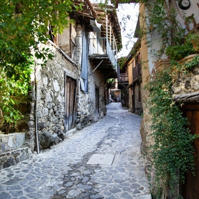 Rua estreita de pedra em vila antiga com vegetação e casas de pedra e madeira