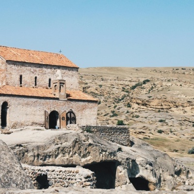 Igreja de pedra com telhado vermelho num terreno rochoso árido.