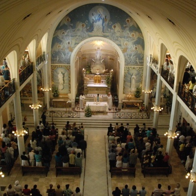 Interior de igreja com teto abobadado, altares decorados e pessoas em cerimónia