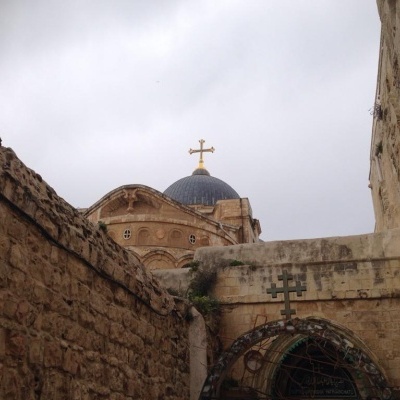 Construção em pedra com cúpula azul e cruz dourada, vista entre paredes de pedra