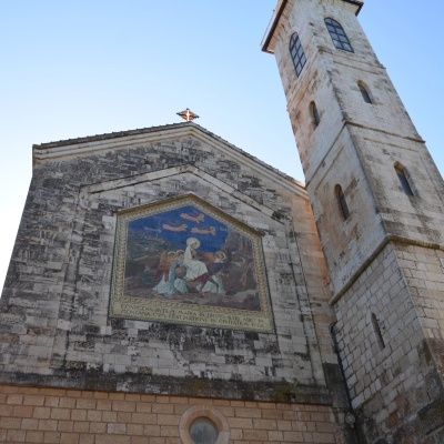 Fachada de igreja em pedra clara com torre e mosaico religioso colorido