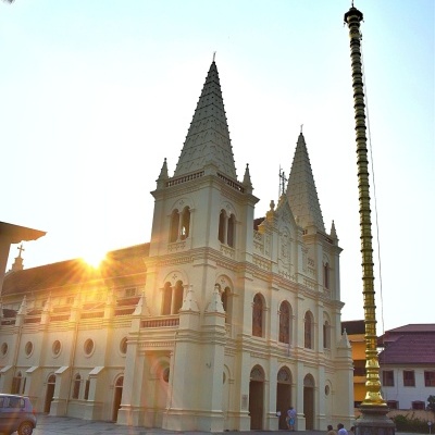 Igreja branca com duas torres pontiagudas e mastro dourado ao lado ao pôr do sol