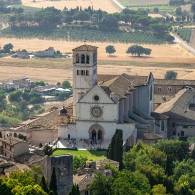 Igreja antiga com torre e jardim, em zona rural com campos agrícolas e casas ao fundo