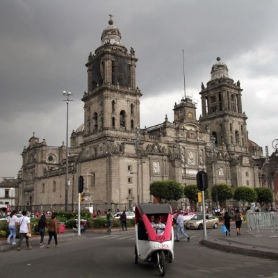Edifício histórico em pedra com torres e pessoas na rua com veículos