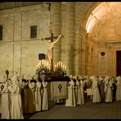 Procissão religiosa noturna com andor de Cristo crucificado e participantes com túnicas brancas