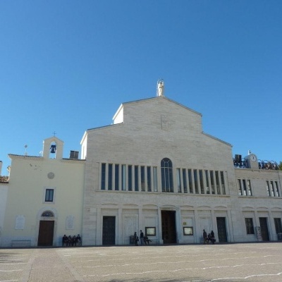 Igreja grande de cor clara com janelas verticais e praça em frente