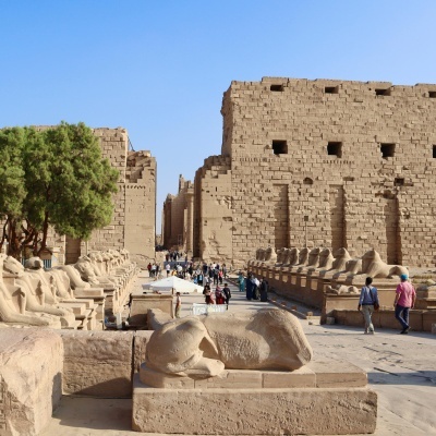 Ruínas antigas com esculturas de esfinges em pedra e pessoas a caminhar