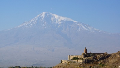 Castelo antigo com igreja sob uma grande montanha nevada e céu azul.