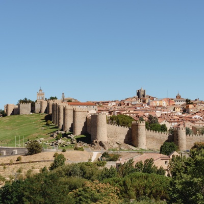 Muralha medieval de pedra com torres e cidade ao fundo sob céu azul