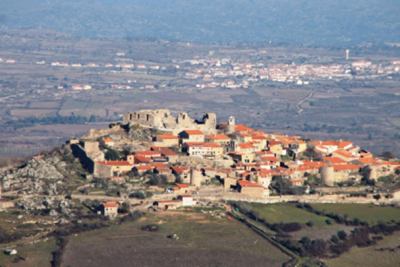 Vista aérea de vila histórica em colina com telhados vermelhos e paisagem rural