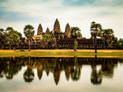 Templo Angkor Wat refletido na água sob céu nublado