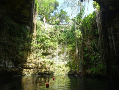 Cenote natural com água clara e vegetação nas paredes rochosas