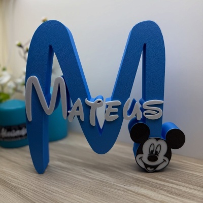 Objeto decorativo azul em forma da letra M com o nome Mateus e cara do Mickey Mouse
