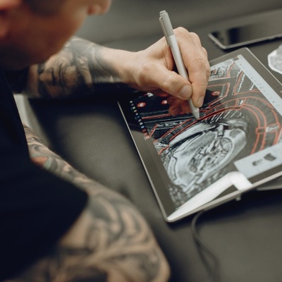 Tablet com ecrã táctil a mostrar desenho de tatuagem, mão com caneta digital a desenhar.