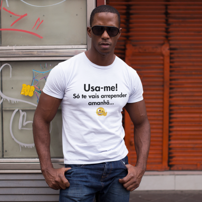 Homem de pele escura com t-shirt branca estampada, jeans e óculos escuros em ambiente urbano com grafitis.