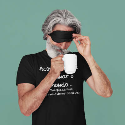 Homem com máscara de dormir preta e caneca branca, vestido com t-shirt preta com texto branco.