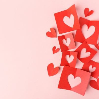 Recortes de papel vermelho com corações recortados e em relevo sobre fundo rosa claro