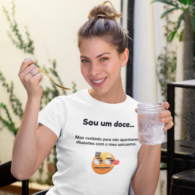 Mulher com t-shirt branca com texto e emoji, segura copo de água e colher dourada