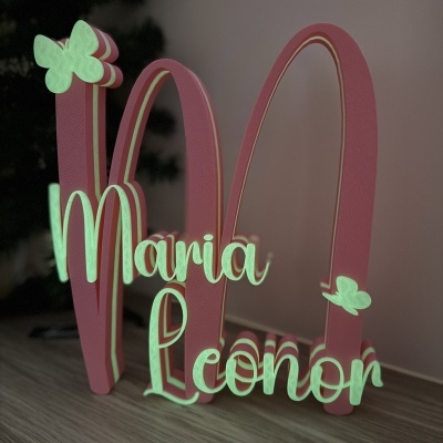 Decoração em madeira com o nome Maria Leonor em letras luminosas verdes e estrutura rosa com borboletas.