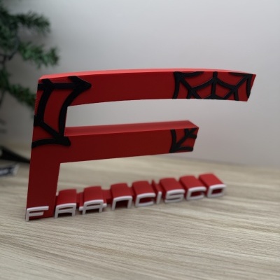 Objeto decorativo vermelho com teias de aranha pretas e texto Francisco em letras brancas