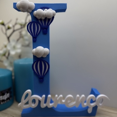 Objeto decorativo azul com a letra L, balões e nome Lourenço branco