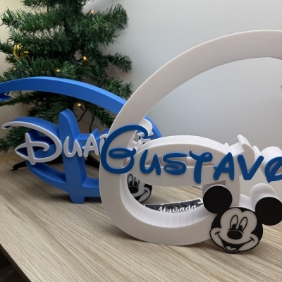 Nomes tridimensionais Disney Duke e Gustavo com decoração de Mickey Mouse e árvore de Natal ao fundo